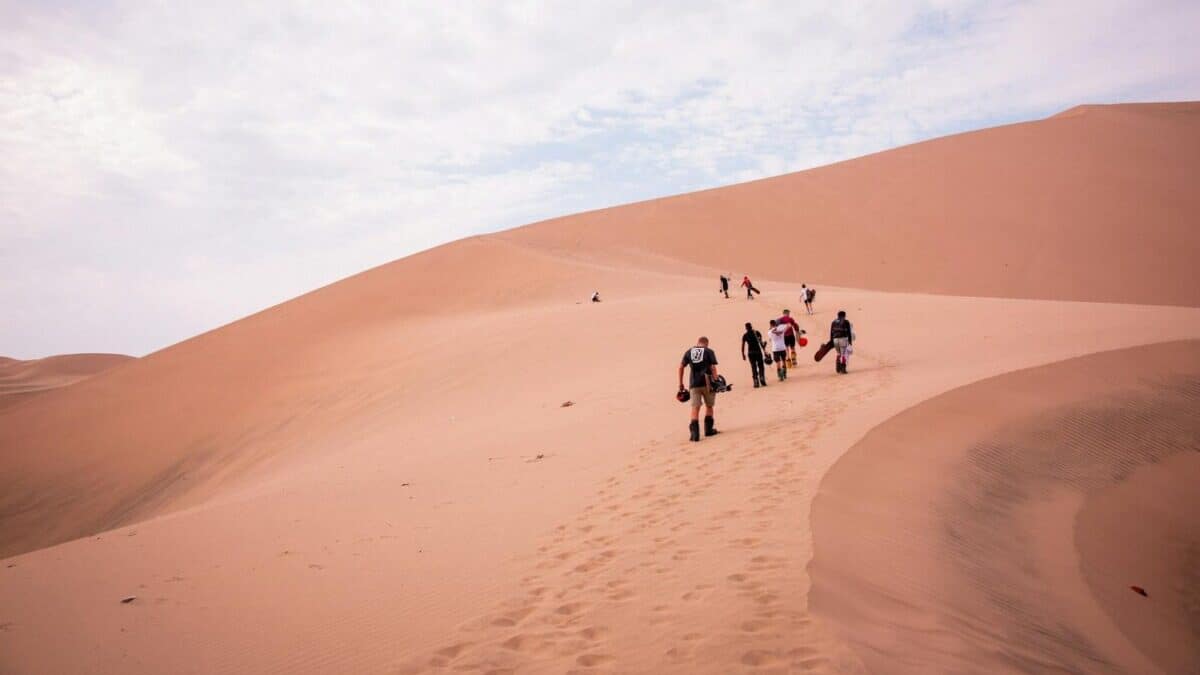 A group of people enjoys sandboarding on the vast dunes of Ica Desert, Peru.