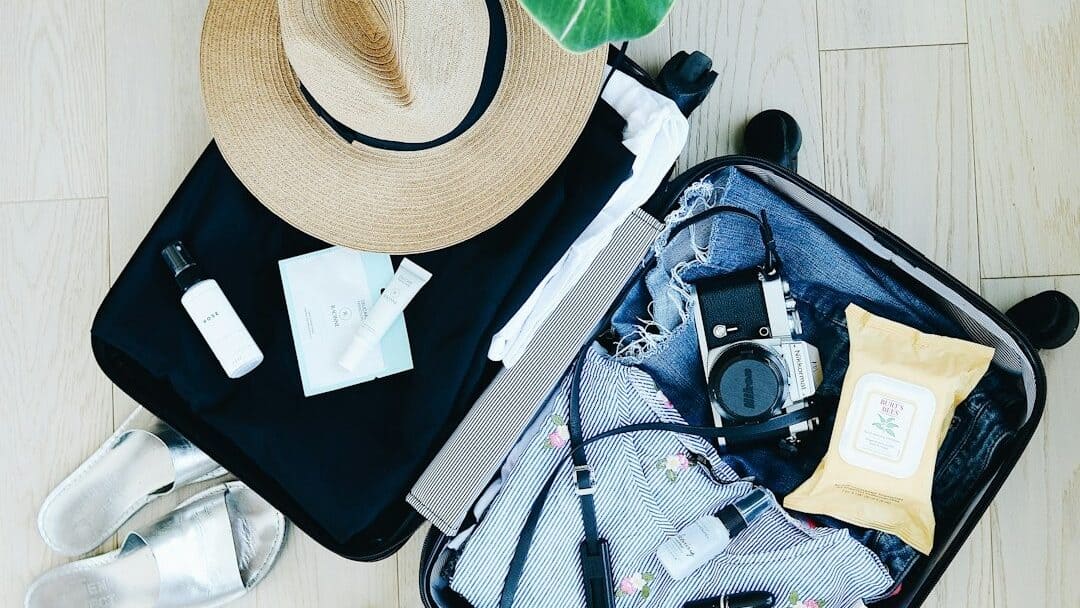 open compact suitcase with packed clothing, accessories, and a hat