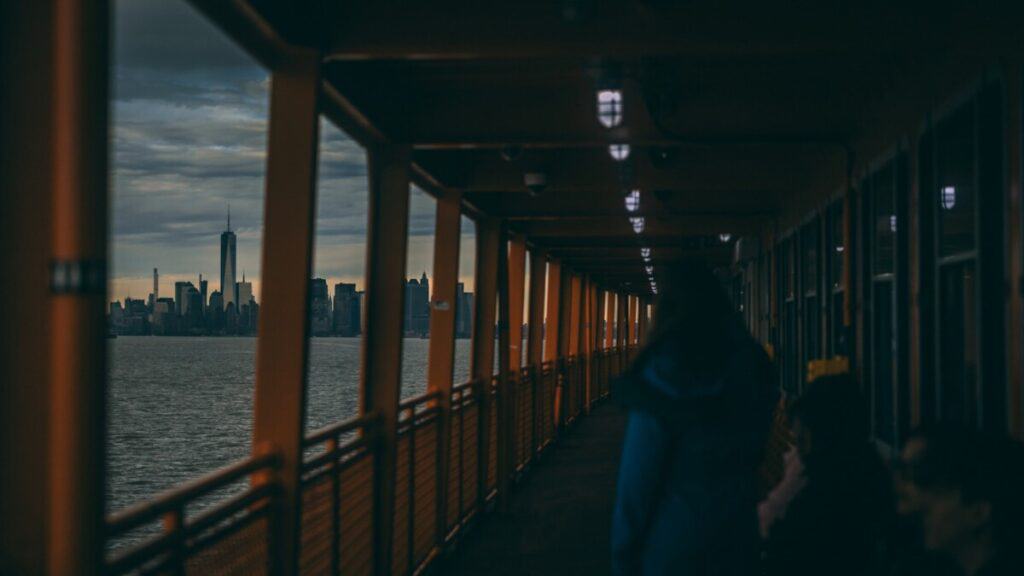 a group of people walking down a walkway next to a body of water, Staten Island Ferry in NYC